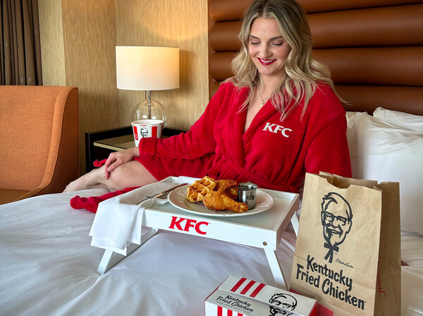 beautiful woman is in a kfc robe sitting on a hotel bed about to eat chicken and waffles